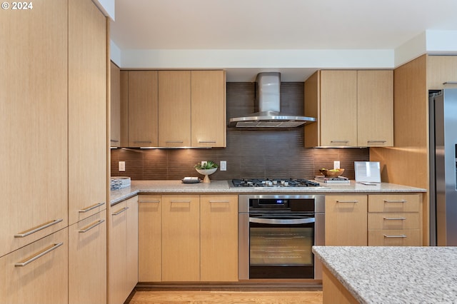 kitchen with light brown cabinetry, wall chimney range hood, and appliances with stainless steel finishes