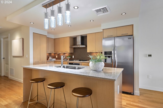 kitchen featuring light wood-type flooring, wall chimney range hood, light stone counters, and stainless steel appliances