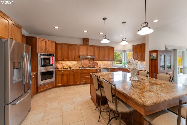 kitchen featuring pendant lighting, a center island, light stone countertops, appliances with stainless steel finishes, and a kitchen bar