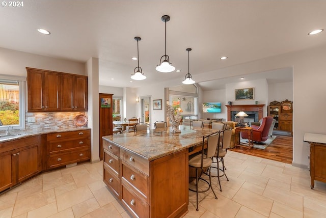 kitchen featuring pendant lighting, a breakfast bar, a center island, decorative backsplash, and light stone counters