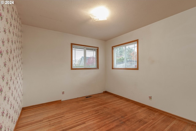 empty room with light wood-type flooring and a textured ceiling