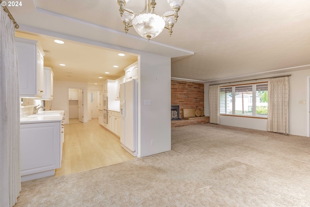 unfurnished living room featuring a chandelier, light carpet, a stone fireplace, and sink