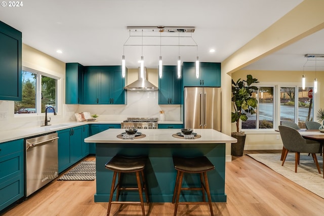 kitchen featuring pendant lighting, a center island, wall chimney range hood, light hardwood / wood-style floors, and stainless steel appliances