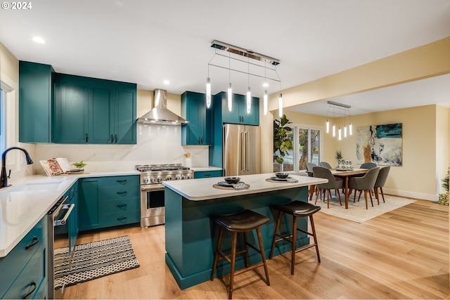 kitchen featuring wall chimney exhaust hood, premium appliances, sink, a center island, and light hardwood / wood-style floors