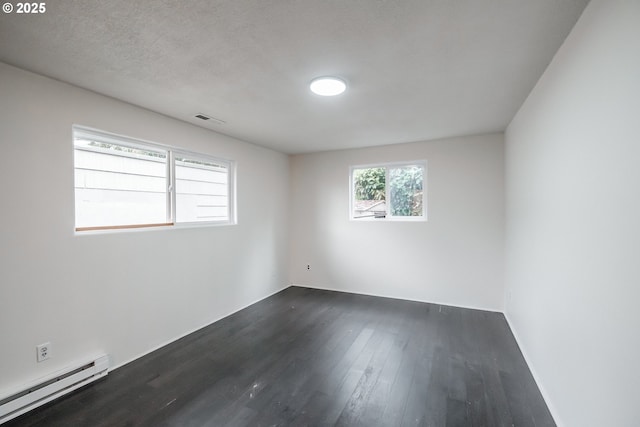 empty room with a textured ceiling, dark hardwood / wood-style flooring, and a baseboard heating unit