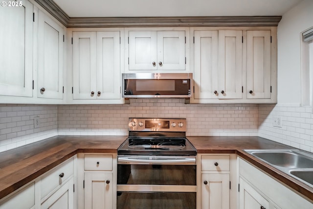 kitchen with butcher block counters, backsplash, sink, appliances with stainless steel finishes, and white cabinetry