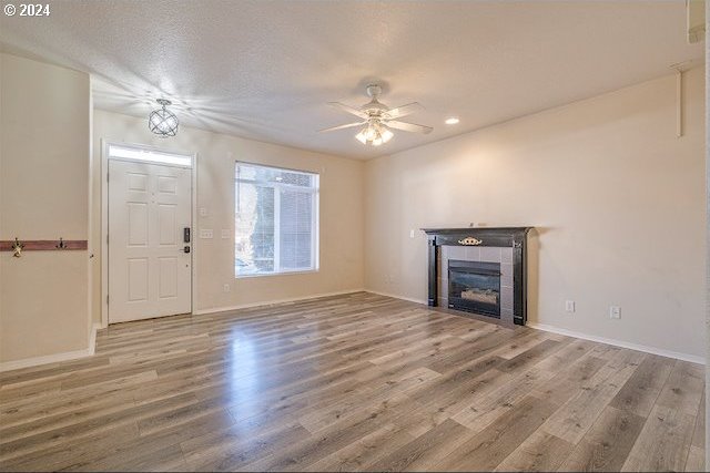 unfurnished living room featuring a textured ceiling, hardwood / wood-style floors, a tiled fireplace, and ceiling fan