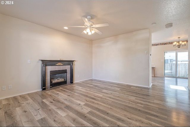 unfurnished living room featuring ceiling fan with notable chandelier, a tiled fireplace, wood-type flooring, and a textured ceiling