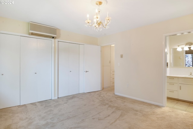 unfurnished bedroom featuring a notable chandelier, light carpet, connected bathroom, a wall mounted AC, and two closets