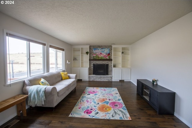 living room featuring built in shelves, a textured ceiling, dark wood-type flooring, and a brick fireplace