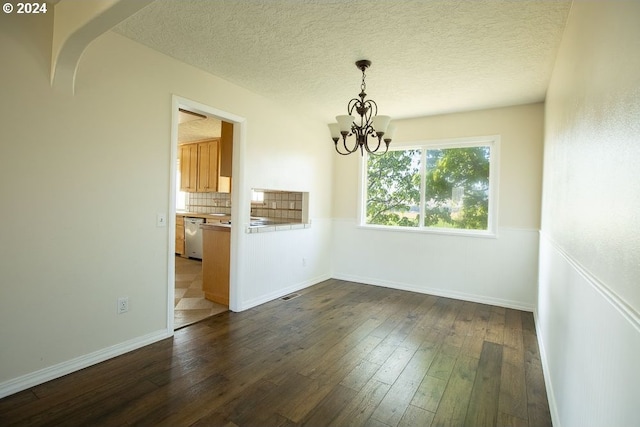 unfurnished dining area featuring a textured ceiling, a notable chandelier, and dark hardwood / wood-style floors