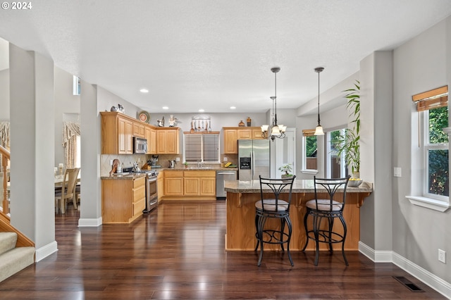 kitchen featuring appliances with stainless steel finishes, dark hardwood / wood-style floors, tasteful backsplash, light stone counters, and an inviting chandelier