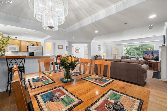 dining space with ornamental molding, light hardwood / wood-style flooring, a raised ceiling, and a chandelier