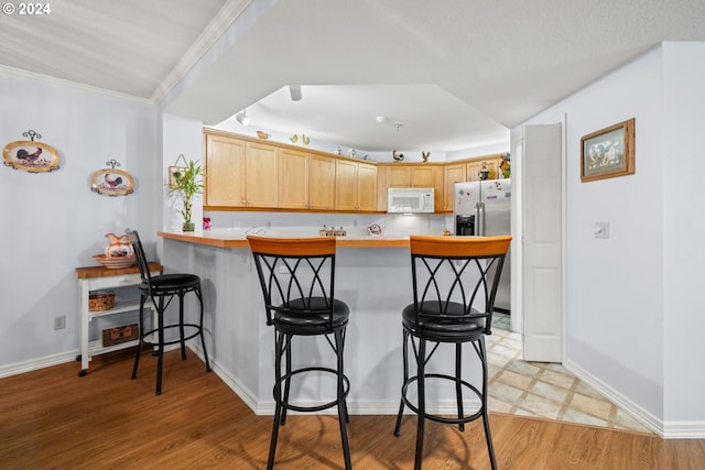 kitchen with stainless steel fridge, a kitchen bar, kitchen peninsula, and light wood-type flooring