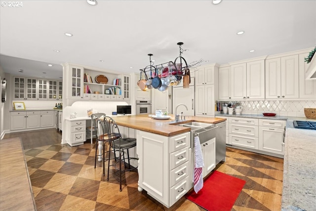 kitchen featuring sink, a breakfast bar area, a center island with sink, stainless steel appliances, and butcher block countertops