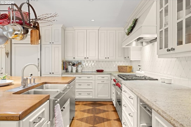 kitchen featuring tasteful backsplash, premium range hood, white cabinetry, and light stone countertops