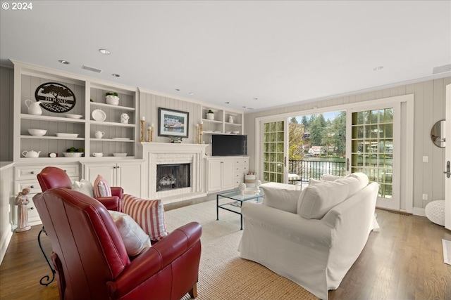 living room with ornamental molding, built in shelves, and light hardwood / wood-style flooring