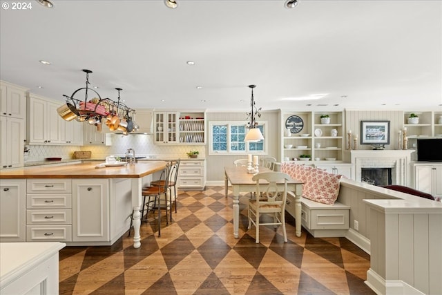 kitchen with pendant lighting, backsplash, wooden counters, a center island with sink, and a kitchen bar