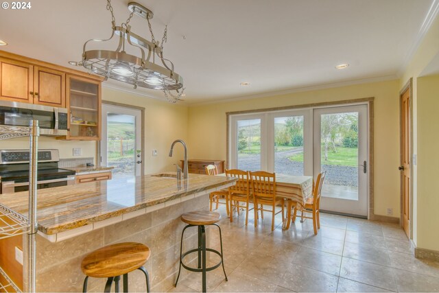 kitchen with stainless steel appliances, light tile floors, ornamental molding, a kitchen bar, and sink