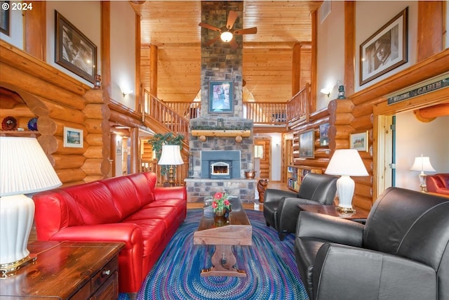 living room with ceiling fan, a towering ceiling, log walls, and a stone fireplace