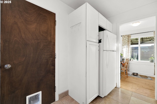 kitchen with white refrigerator, light tile patterned flooring, and white cabinets