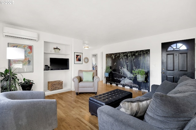 living room with hardwood / wood-style floors, built in shelves, and a wall mounted air conditioner