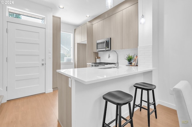 kitchen featuring kitchen peninsula, a breakfast bar area, light wood-type flooring, pendant lighting, and sink