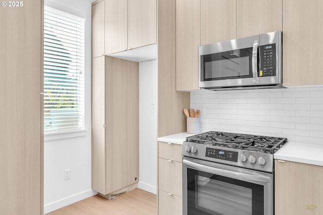 kitchen featuring light wood-type flooring, appliances with stainless steel finishes, decorative backsplash, and light brown cabinets