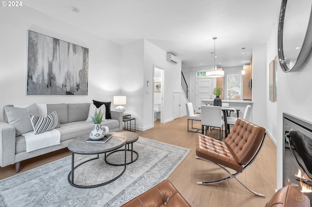 living room with a wall mounted AC, a fireplace, and light hardwood / wood-style flooring