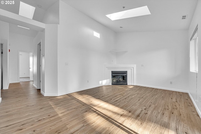 unfurnished living room featuring a skylight, high vaulted ceiling, and light wood-type flooring