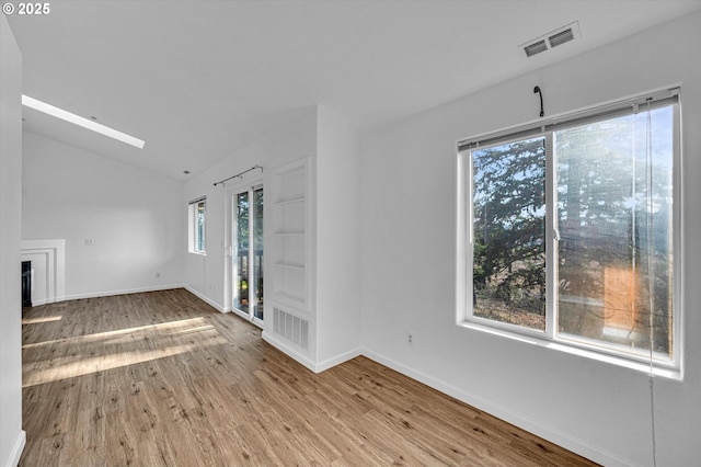 unfurnished living room with vaulted ceiling with skylight and light wood-type flooring