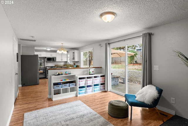 kitchen with appliances with stainless steel finishes, light wood-type flooring, decorative light fixtures, an inviting chandelier, and white cabinets