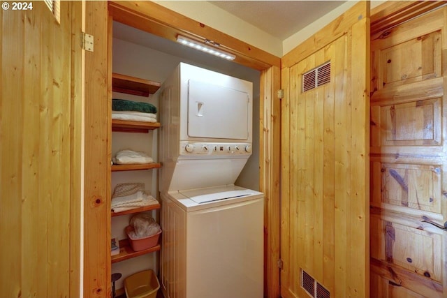 laundry room featuring stacked washer and clothes dryer and wooden walls