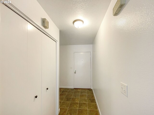 corridor featuring a textured ceiling and dark tile patterned floors