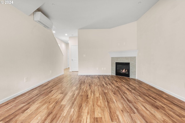 unfurnished living room featuring light wood-type flooring, a wall unit AC, and a tiled fireplace