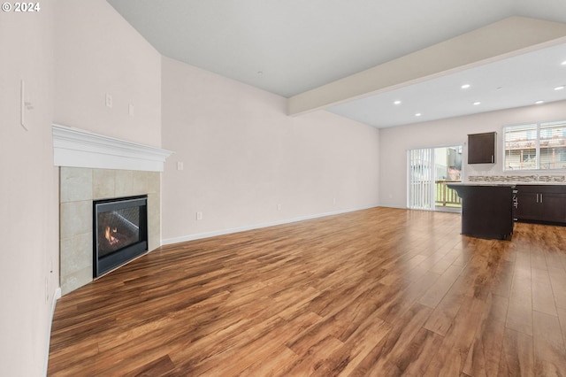 unfurnished living room with a tiled fireplace, hardwood / wood-style floors, and beamed ceiling