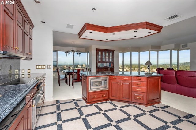 kitchen featuring ceiling fan, a raised ceiling, black electric stovetop, a center island, and stainless steel microwave