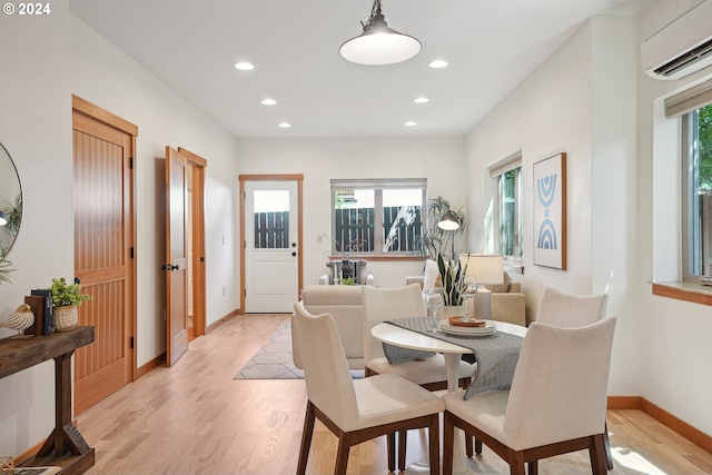 dining room with a wall unit AC, a wealth of natural light, and light hardwood / wood-style floors