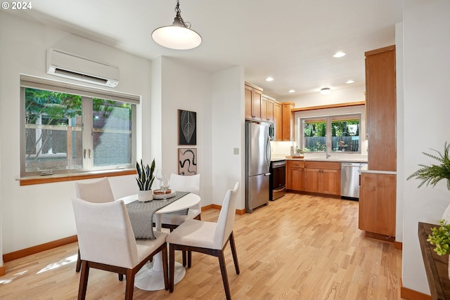 kitchen with a wall unit AC, light wood-type flooring, sink, hanging light fixtures, and appliances with stainless steel finishes