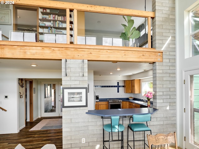 kitchen with sink, electric stove, a kitchen bar, backsplash, and dark hardwood / wood-style flooring