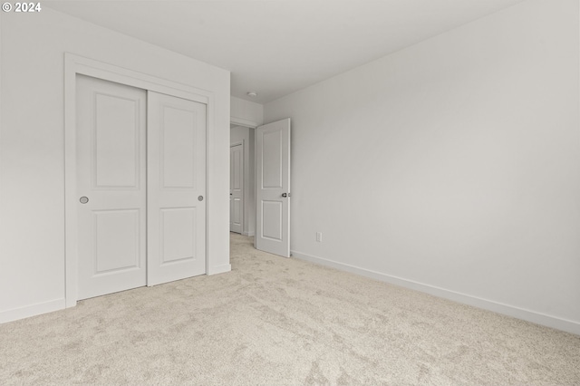 unfurnished bedroom with light colored carpet and a closet