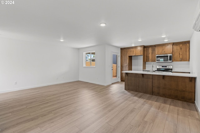 kitchen with a kitchen breakfast bar, stainless steel appliances, light hardwood / wood-style floors, and sink