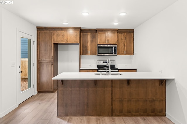 kitchen with appliances with stainless steel finishes, kitchen peninsula, sink, and light wood-type flooring