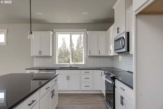 kitchen featuring white cabinets, appliances with stainless steel finishes, decorative light fixtures, and backsplash