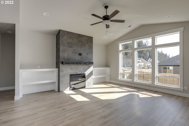 unfurnished living room featuring a tiled fireplace, a healthy amount of sunlight, ceiling fan, and light hardwood / wood-style flooring