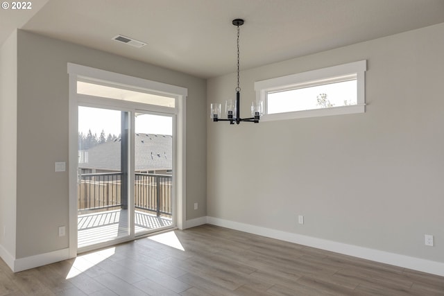 empty room with light hardwood / wood-style flooring and an inviting chandelier