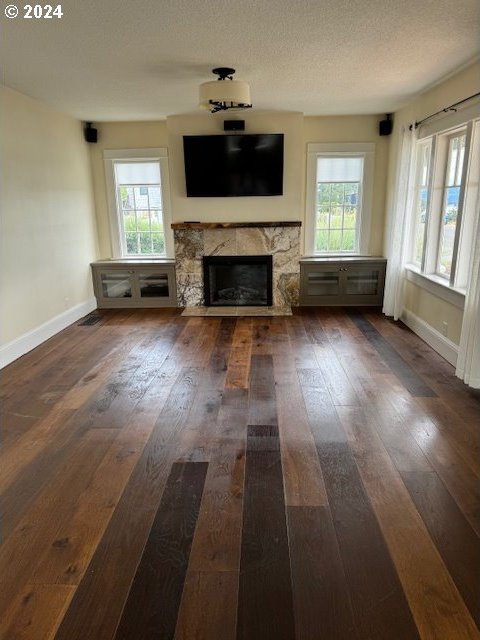 unfurnished living room with dark hardwood / wood-style floors, a textured ceiling, a stone fireplace, and a wealth of natural light