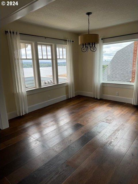 unfurnished dining area with wood-type flooring, a textured ceiling, and an inviting chandelier