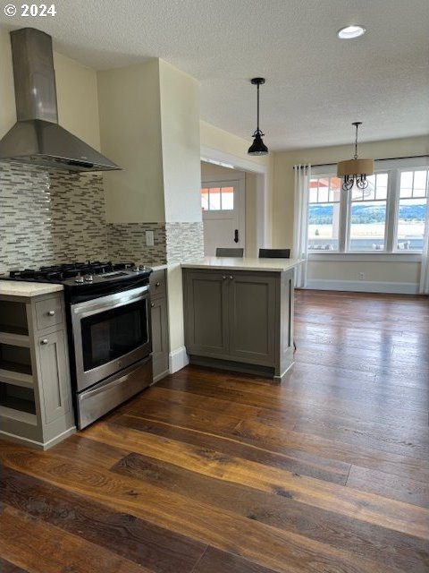 kitchen with pendant lighting, wall chimney range hood, gray cabinetry, stainless steel gas range oven, and kitchen peninsula