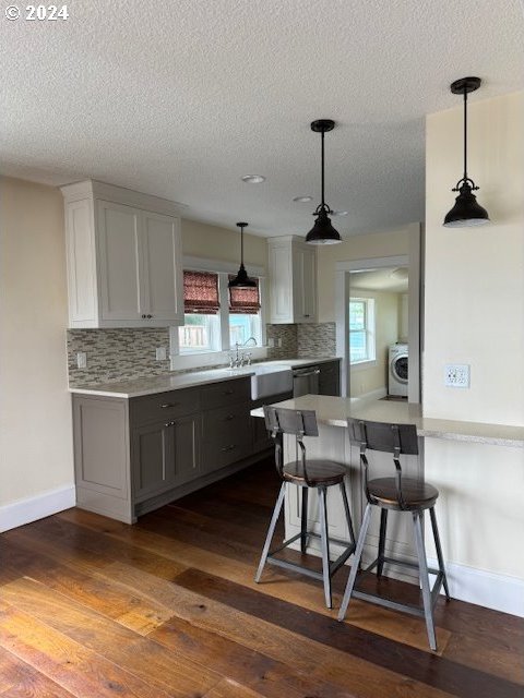 kitchen with dark wood-type flooring, gray cabinetry, a kitchen breakfast bar, washer / dryer, and kitchen peninsula